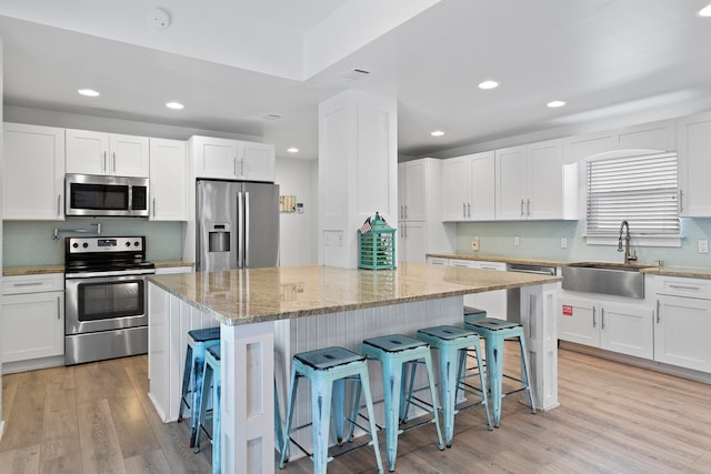 kitchen with sink, white cabinetry, stainless steel appliances, a breakfast bar, and light hardwood / wood-style floors