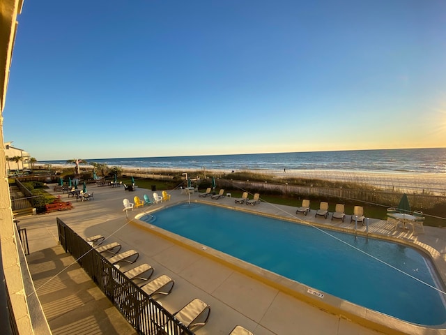 view of swimming pool with a water view, a beach view, and a patio area