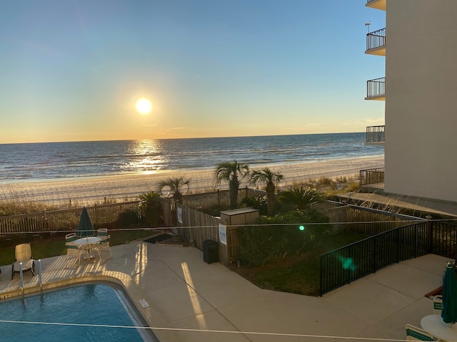 pool at dusk with a view of the beach, a water view, and a patio area