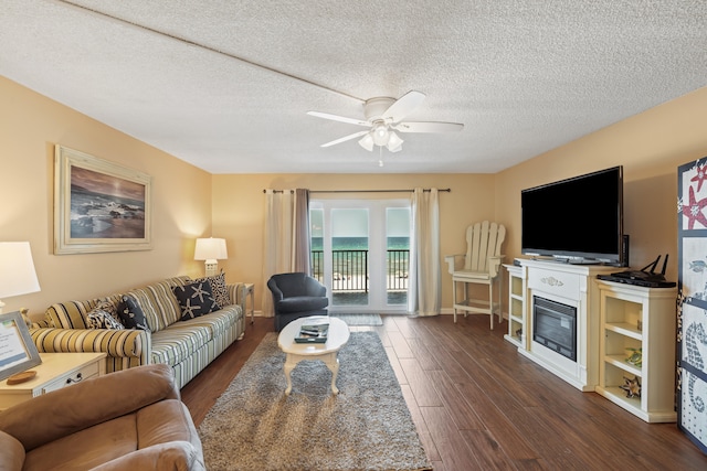 living room with ceiling fan, a textured ceiling, and dark wood-type flooring