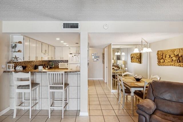 kitchen with white cabinets, white appliances, kitchen peninsula, light tile patterned floors, and decorative light fixtures