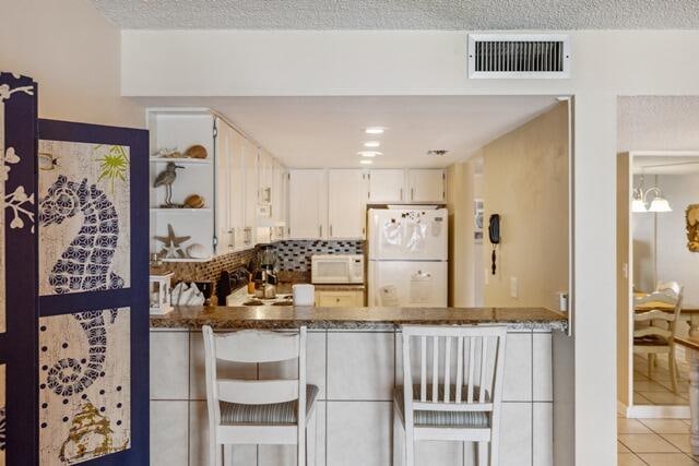 kitchen featuring dark stone counters, white cabinets, white appliances, and a kitchen bar