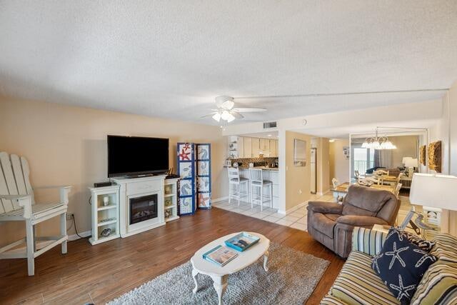 living room with ceiling fan with notable chandelier, a textured ceiling, and hardwood / wood-style floors