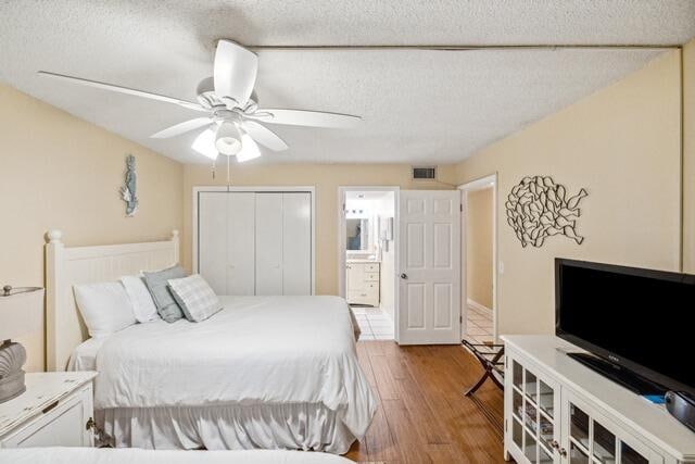 bedroom featuring ceiling fan, a textured ceiling, light hardwood / wood-style flooring, a closet, and ensuite bath