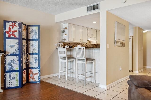 kitchen featuring white refrigerator, a textured ceiling, white cabinets, light hardwood / wood-style flooring, and backsplash