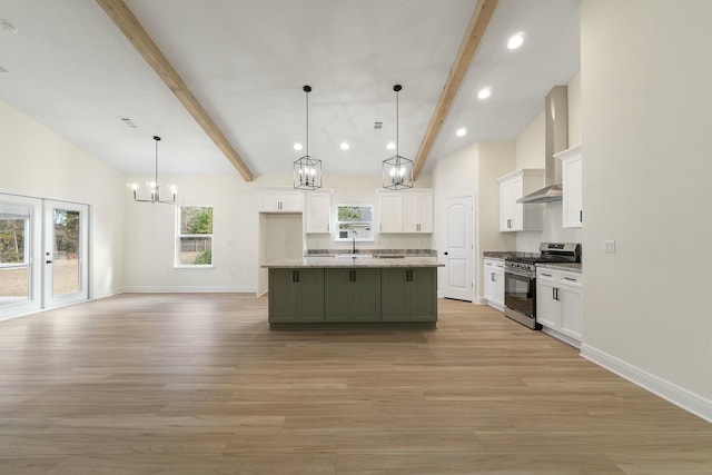 kitchen with stainless steel gas stove, wall chimney range hood, a kitchen island with sink, and light hardwood / wood-style flooring