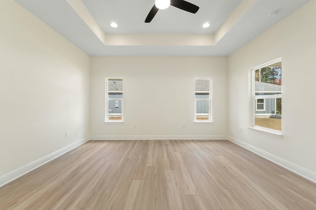 unfurnished room featuring a tray ceiling, ceiling fan, and light hardwood / wood-style floors