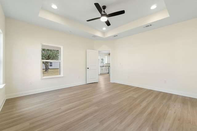 unfurnished room with a raised ceiling, ceiling fan, and light hardwood / wood-style flooring