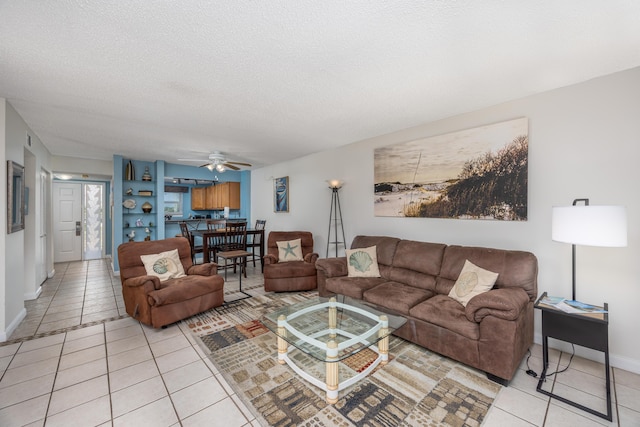living area featuring baseboards, light tile patterned floors, a ceiling fan, and a textured ceiling
