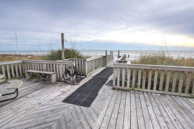 wooden terrace featuring a beach view and a water view