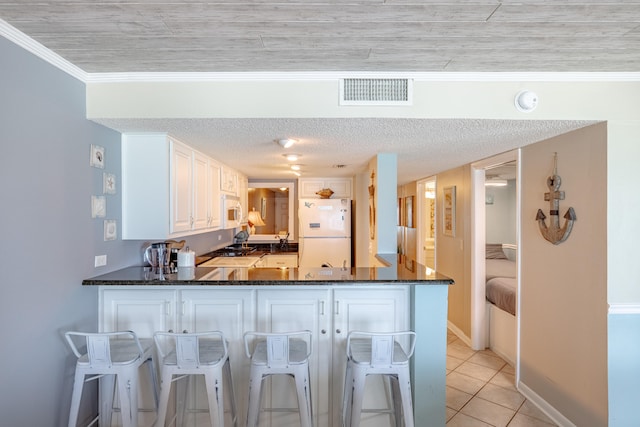 kitchen featuring dark stone countertops, light tile patterned flooring, white cabinets, white appliances, and kitchen peninsula