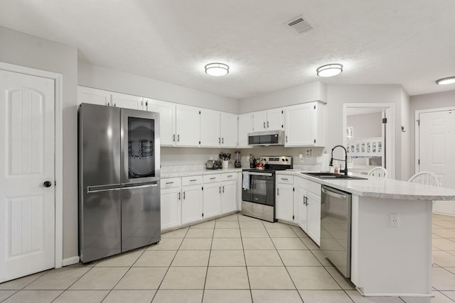 kitchen featuring a textured ceiling, light tile patterned floors, stainless steel appliances, and white cabinets