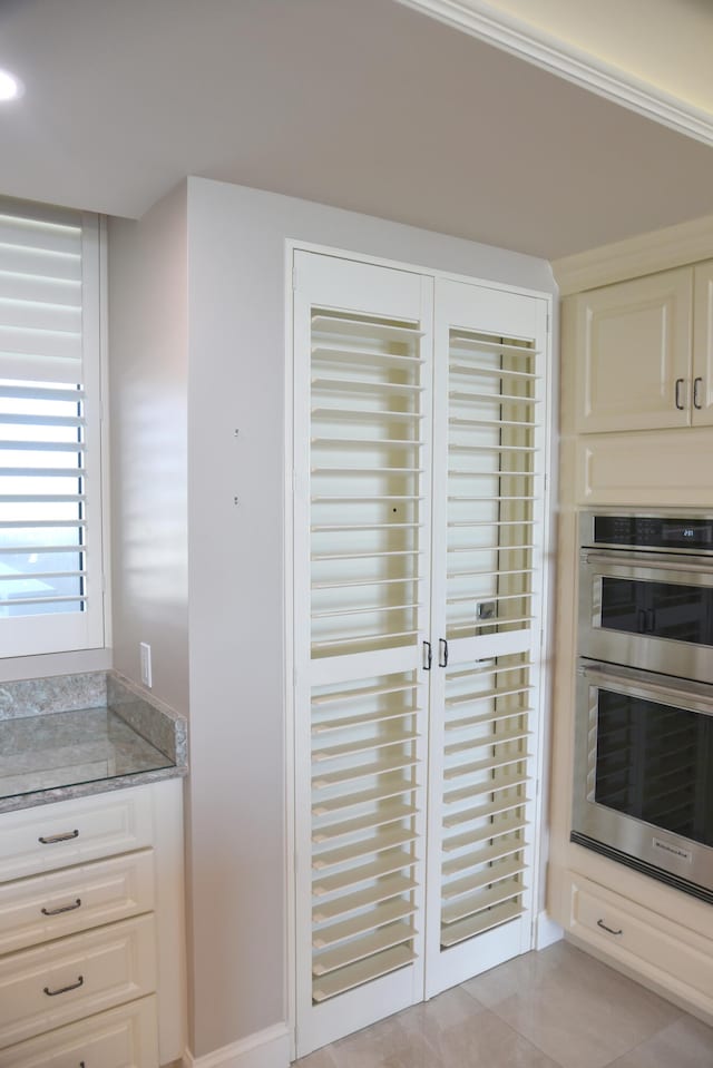 kitchen featuring stainless steel double oven, light stone counters, and light tile patterned floors