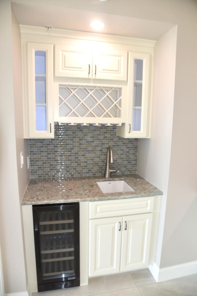 bar featuring wine cooler, sink, light stone counters, decorative backsplash, and white cabinetry