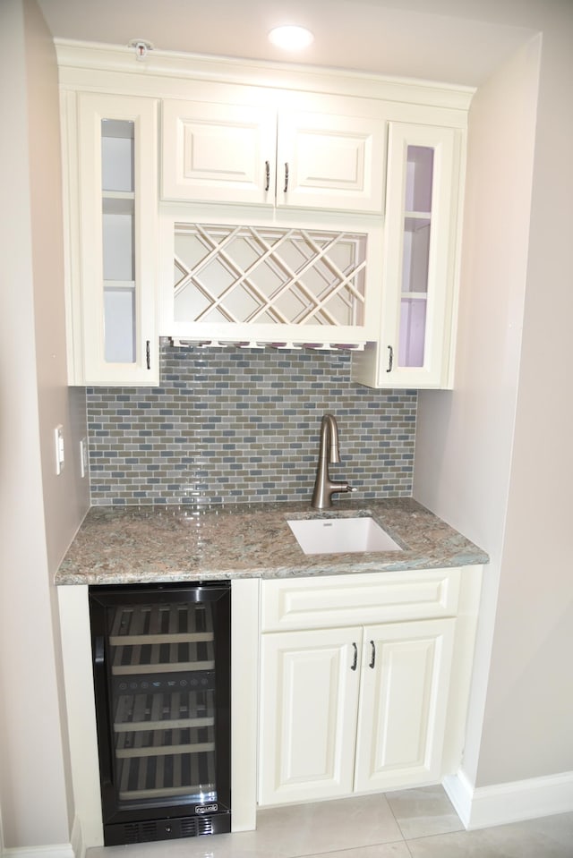 bar with wine cooler, sink, decorative backsplash, light stone countertops, and white cabinetry