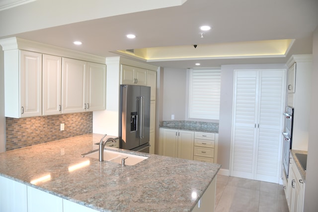 kitchen featuring stainless steel appliances, kitchen peninsula, sink, and light stone counters