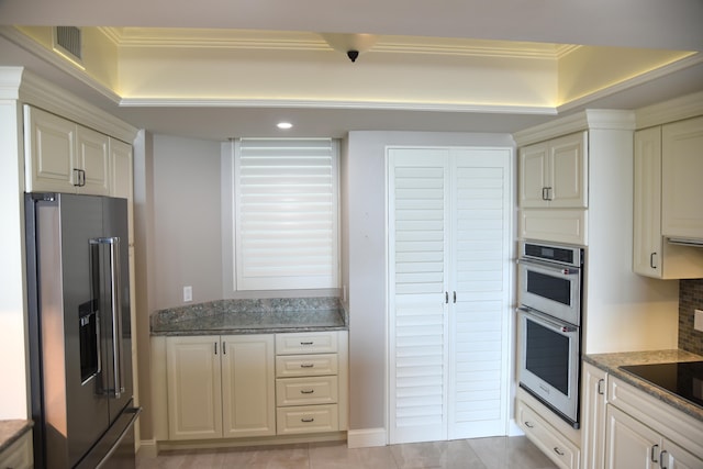 kitchen featuring ornamental molding, cream cabinets, dark stone counters, and stainless steel appliances