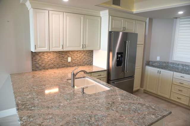 kitchen with light stone countertops, decorative backsplash, stainless steel fridge, sink, and kitchen peninsula