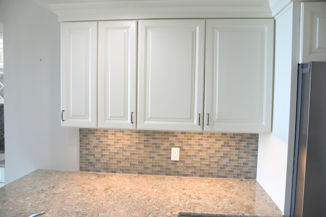 interior space featuring stainless steel refrigerator, light stone countertops, decorative backsplash, and white cabinetry