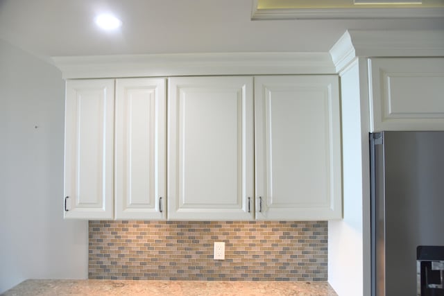 interior details featuring light stone counters, decorative backsplash, stainless steel refrigerator, and white cabinets