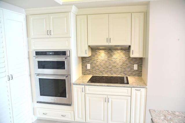 kitchen with light stone countertops, tasteful backsplash, stainless steel double oven, white cabinetry, and black electric stovetop