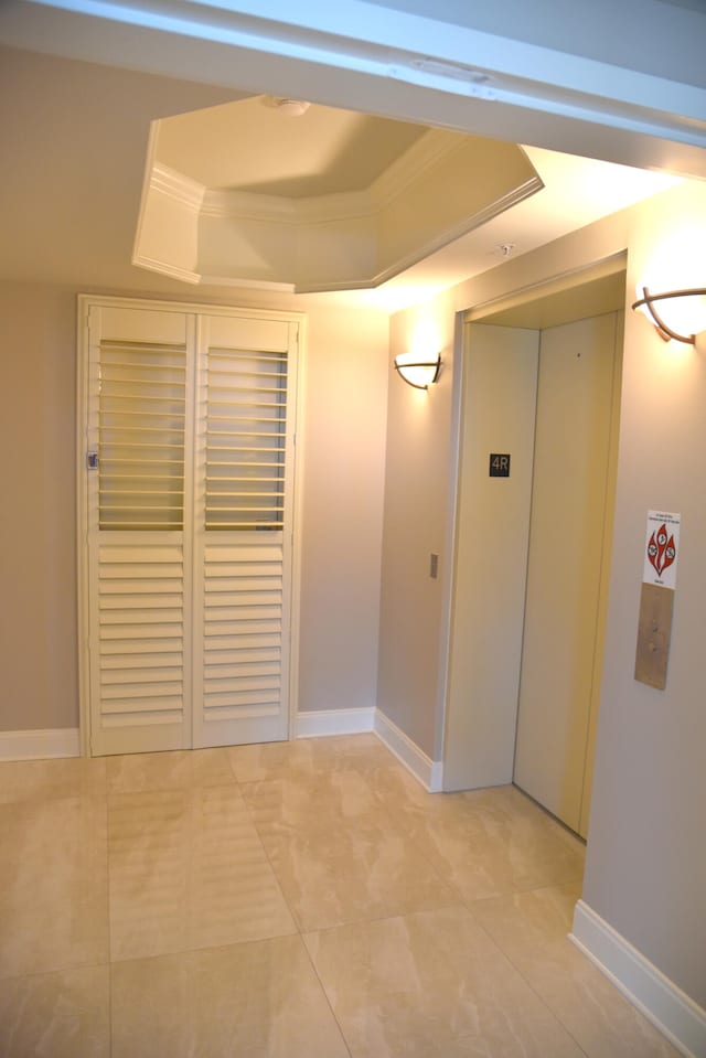 corridor featuring a raised ceiling, ornamental molding, and light tile patterned floors