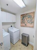 clothes washing area with washing machine and dryer, light tile patterned flooring, and cabinets