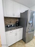 kitchen with backsplash, white cabinetry, and stainless steel refrigerator