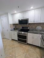 kitchen with white cabinets, appliances with stainless steel finishes, light tile patterned floors, and decorative backsplash