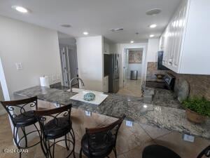 kitchen with stainless steel fridge, white cabinets, kitchen peninsula, stone counters, and stove