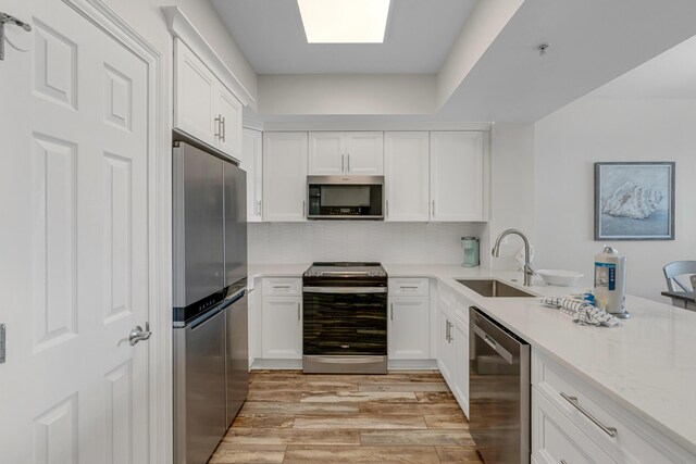 kitchen featuring light stone counters, sink, white cabinetry, light hardwood / wood-style flooring, and appliances with stainless steel finishes