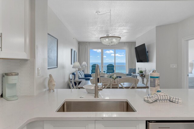 kitchen with a chandelier, a textured ceiling, sink, white cabinets, and decorative backsplash