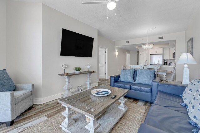 living room with light hardwood / wood-style flooring, a textured ceiling, and ceiling fan with notable chandelier