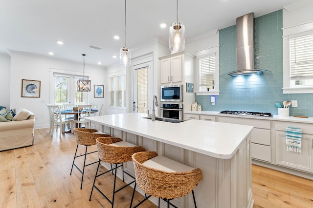 kitchen with wall chimney exhaust hood, light wood-type flooring, white cabinetry, and a center island with sink