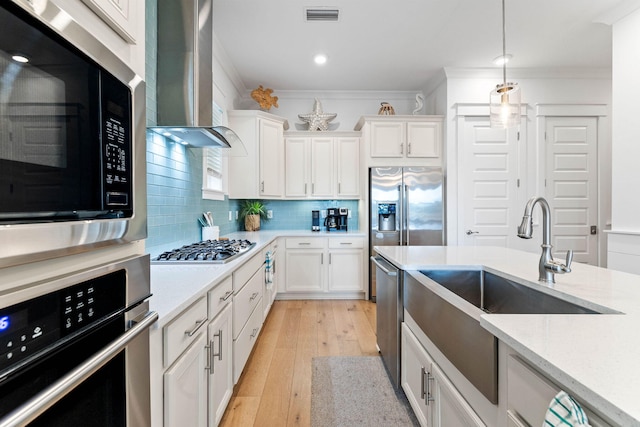 kitchen featuring white cabinets, stainless steel appliances, wall chimney exhaust hood, and light hardwood / wood-style floors