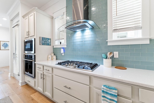 kitchen featuring white cabinetry, wall chimney range hood, stainless steel appliances, and light hardwood / wood-style flooring