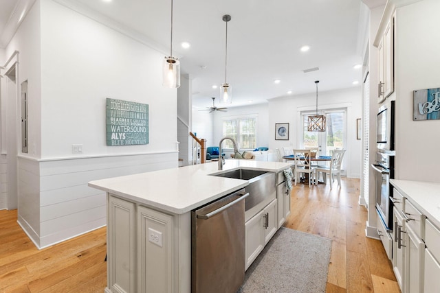 kitchen featuring light wood-type flooring, white cabinetry, a center island with sink, appliances with stainless steel finishes, and ceiling fan