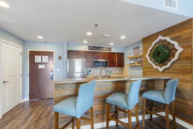 kitchen with light stone counters, dark wood-type flooring, appliances with stainless steel finishes, a kitchen bar, and decorative backsplash