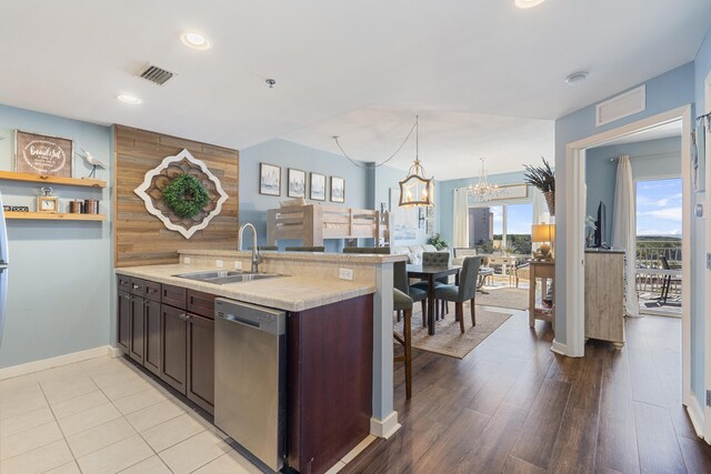 kitchen featuring dark brown cabinetry, sink, stainless steel dishwasher, an inviting chandelier, and light hardwood / wood-style floors