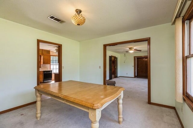 unfurnished dining area featuring light carpet, ceiling fan, and a textured ceiling