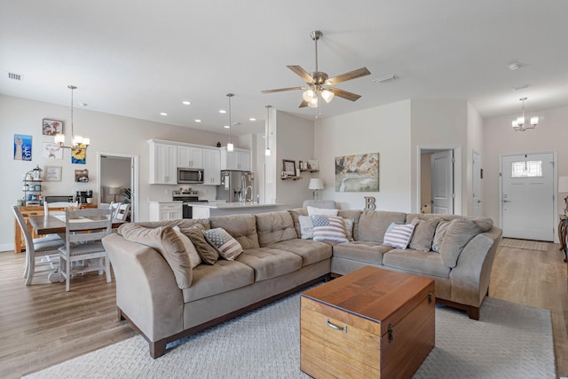 living room with sink, light wood-type flooring, and ceiling fan with notable chandelier