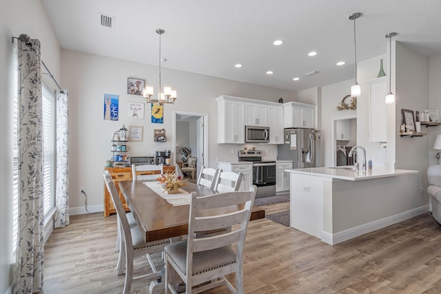 kitchen with kitchen peninsula, hanging light fixtures, appliances with stainless steel finishes, white cabinetry, and light wood-type flooring