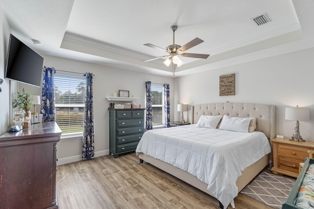 bedroom featuring multiple windows, a tray ceiling, light wood-type flooring, and ceiling fan