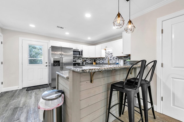 kitchen with light stone counters, a kitchen bar, white cabinetry, stainless steel appliances, and hardwood / wood-style floors