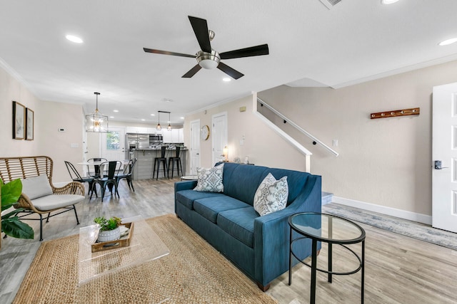 living room featuring light hardwood / wood-style flooring, ceiling fan with notable chandelier, and ornamental molding