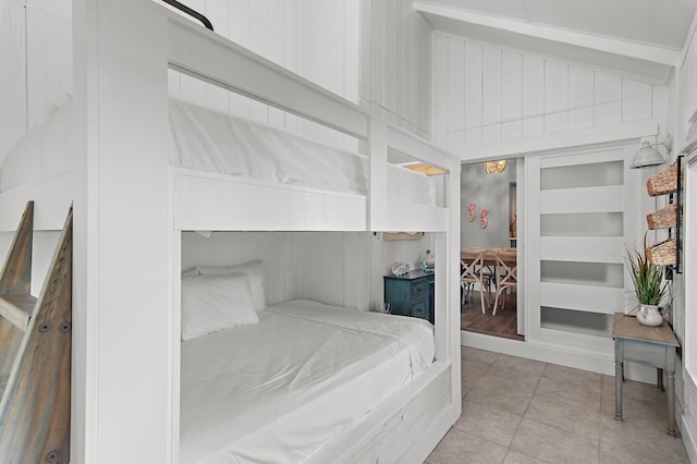 bedroom featuring wood walls, vaulted ceiling, and light tile patterned floors