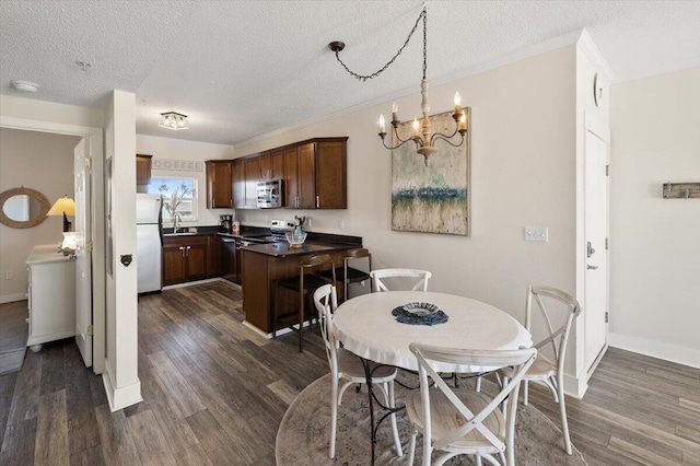 dining space with a textured ceiling, crown molding, dark wood-type flooring, sink, and an inviting chandelier