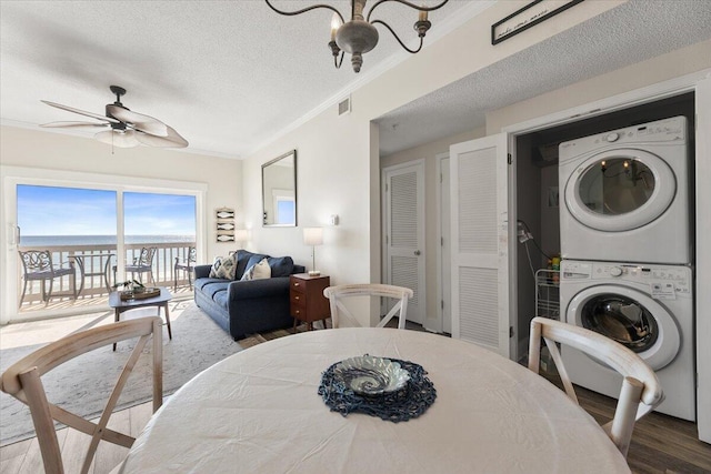 dining area featuring stacked washing maching and dryer, a textured ceiling, ceiling fan, wood-type flooring, and a water view