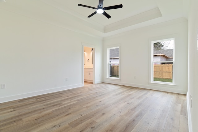 unfurnished bedroom with ceiling fan, light wood-type flooring, ensuite bath, and a tray ceiling