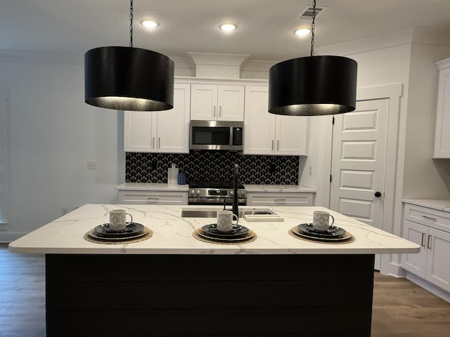 kitchen featuring appliances with stainless steel finishes, white cabinetry, hanging light fixtures, light stone countertops, and a center island with sink